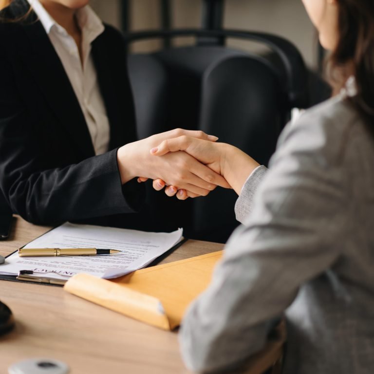 Woman lawyer hand and women client shaking hand collaborate on working agreements with contract documents at the office.
