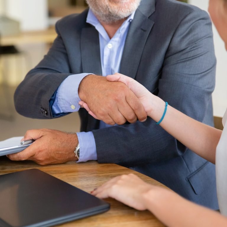 Mature legal advisor meeting with young customer at co-working, holding documents and shaking hands. Cropped shot. Paperwork or collaboration concept